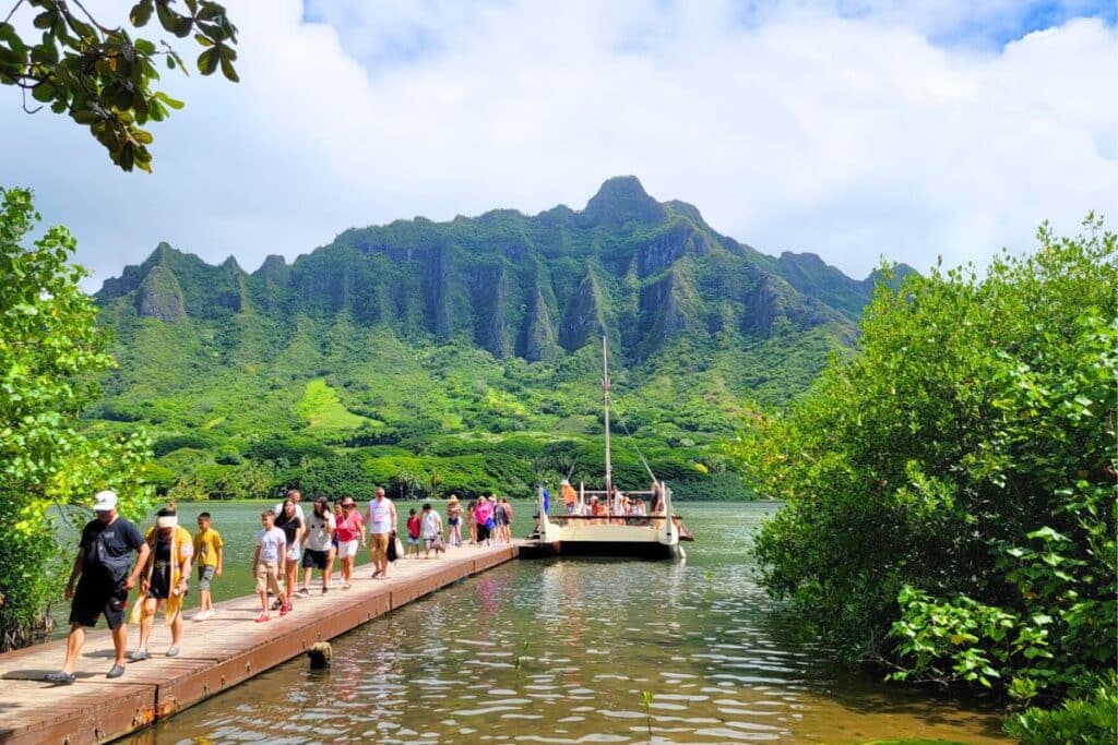 People walking along a wooden dock across a fish pond after getting off a boat at Kualoa Ranch